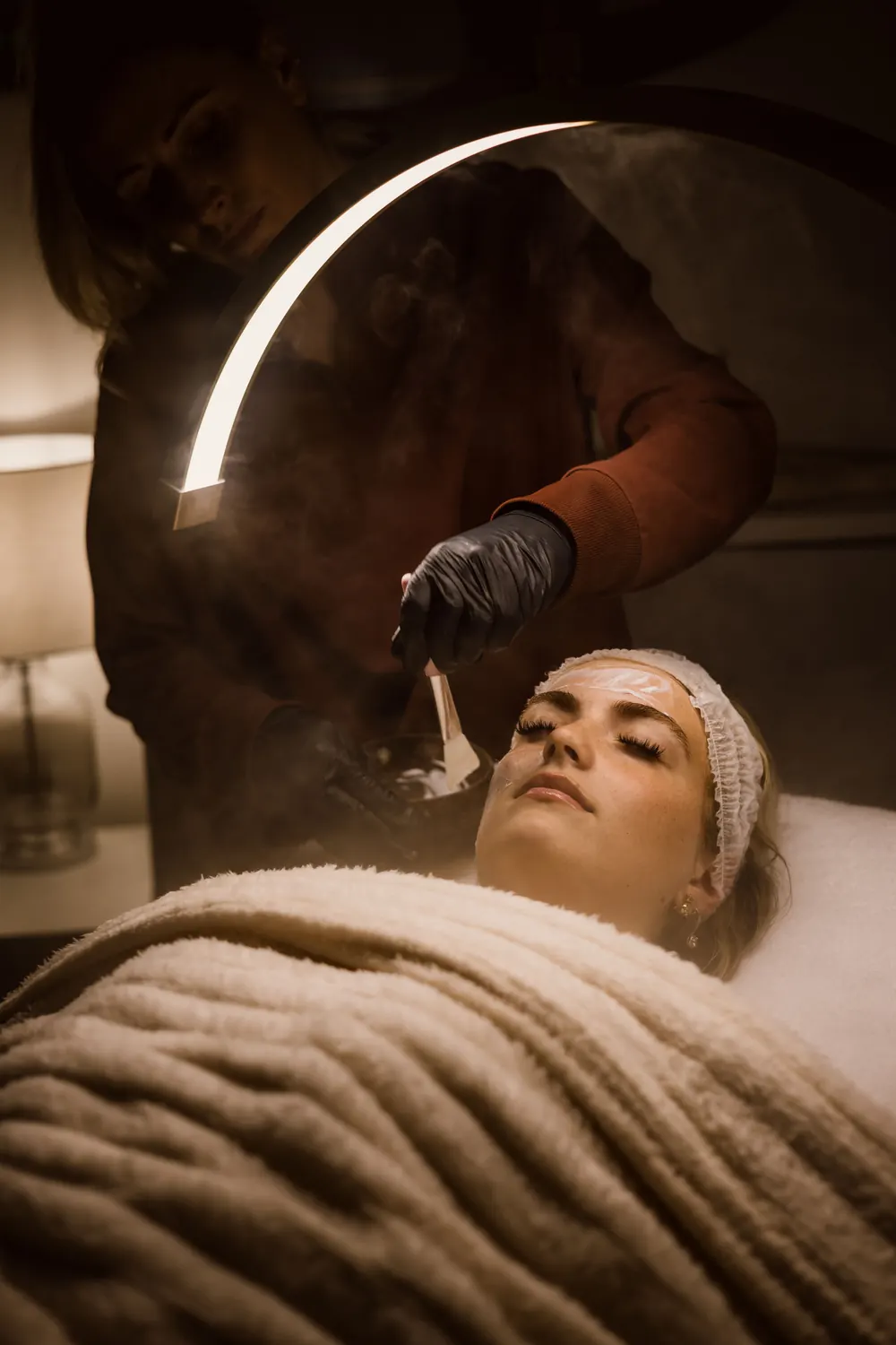 Therapist applying a facial mask with a brush in a softly lit salon